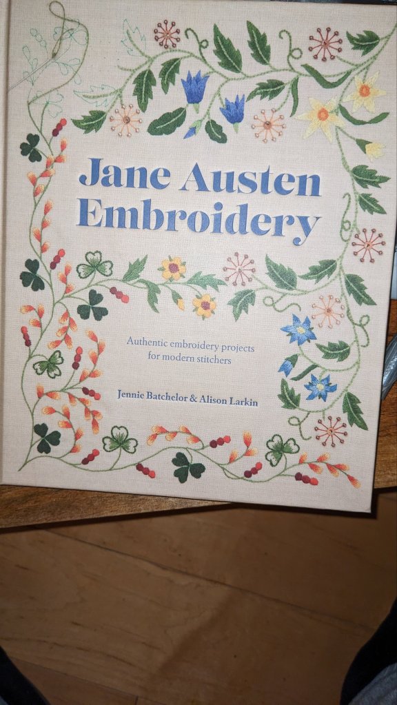 An image of the front cover of the book "Jane Austen Embroidery".  In addition to the title and the author's names the cover is decorated with a wonderful twisting Vine which is decorated with various leaves and flowers in blues reds greens and yellows